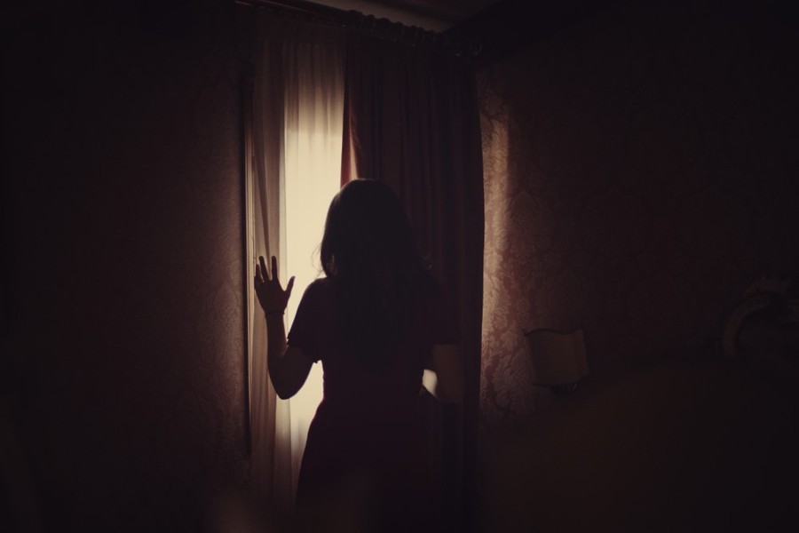 woman looking out window from dark room in venice